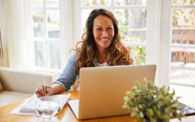 Smiling woman taking notes at a table in front of an open laptop