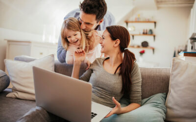 Couple and their young daughter smiling together on a couch around a laptop