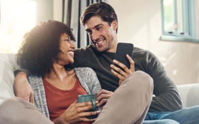 Couple relaxing on a couch at home, the woman holding a mug and the man holding a phone